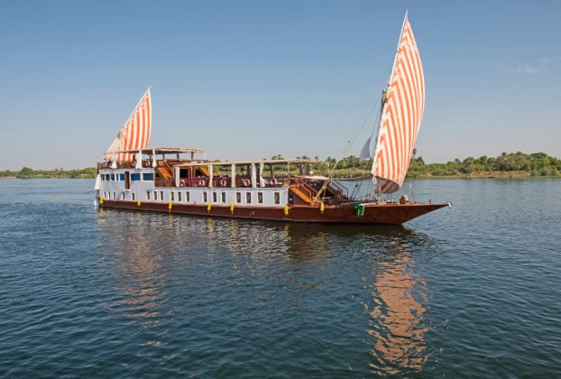 Sailing boat with striped sails on calm waters.
